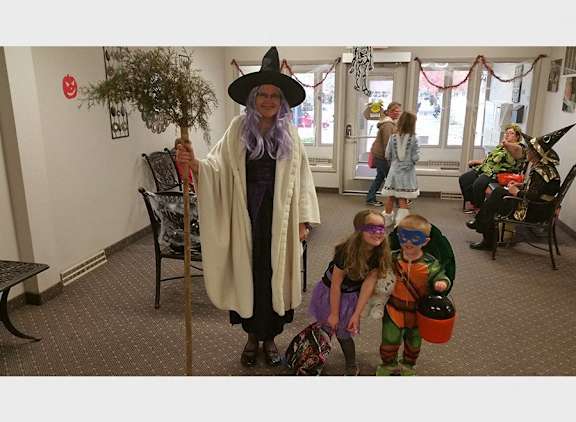 A person in a witch costume stands in a room with children.