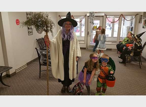 A person in a witch costume stands in a room with children.