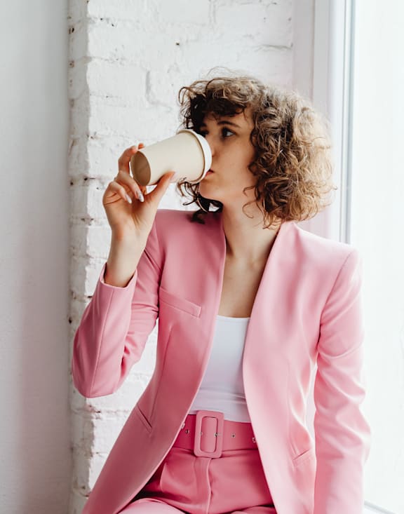 A woman in a pink suit is drinking from a paper cup.