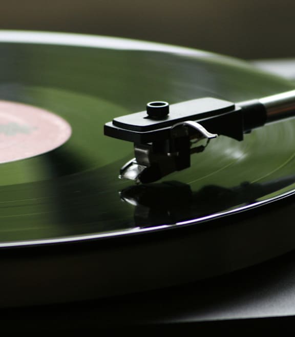 A record player's tonearm is shown in close-up.