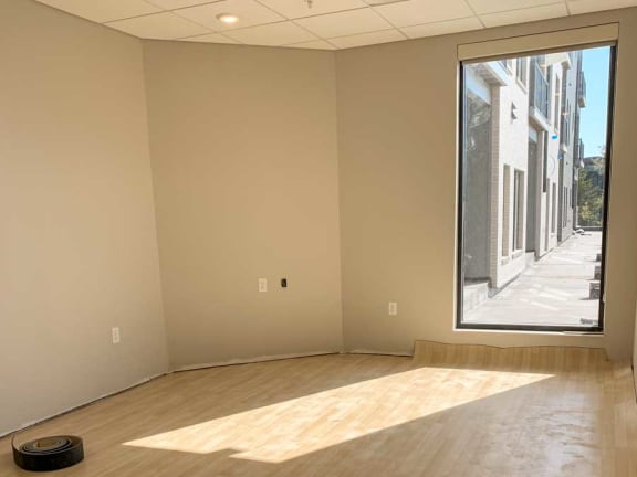 Room with tan wood floors, beige walls, and window looking outside