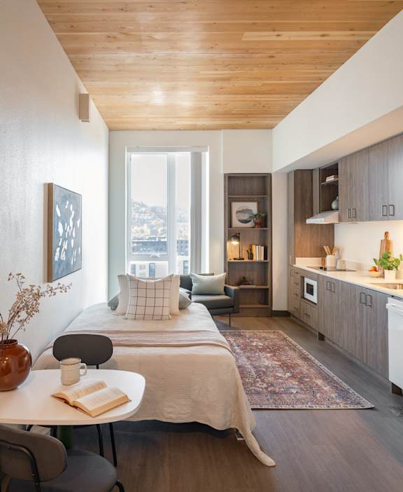A modern bedroom with a bed, a table, a chair, a vase, a book, and a cup on the table.