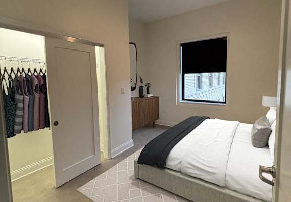 A bedroom with a bed, a dresser, and a window. at The Annex Apartments, Buffalo, NY, 14222