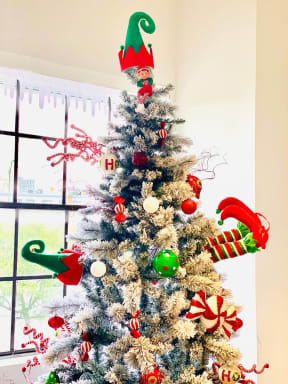 a white christmas tree with elf decorations in a window