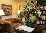 Thumbnail 7 of 11 - A room with a brown couch, a round table with a book on it, and a flower arrangement.