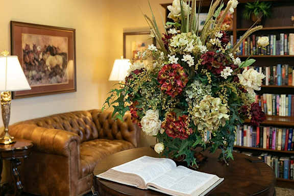 A room with a brown couch, a round table with a book on it, and a flower arrangement.