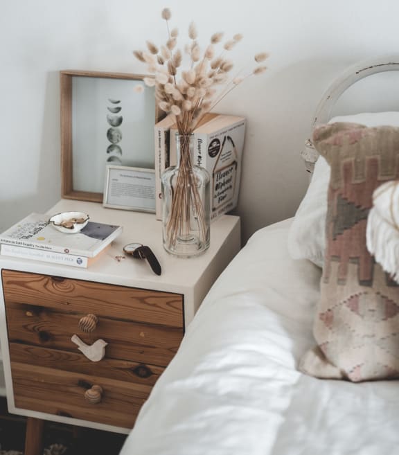 A bedroom with a bed, nightstand, and a vase of flowers on top, creating a cozy atmosphere.