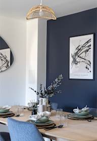 a dining room with a wooden table and blue chairs and a blue wall with artwork