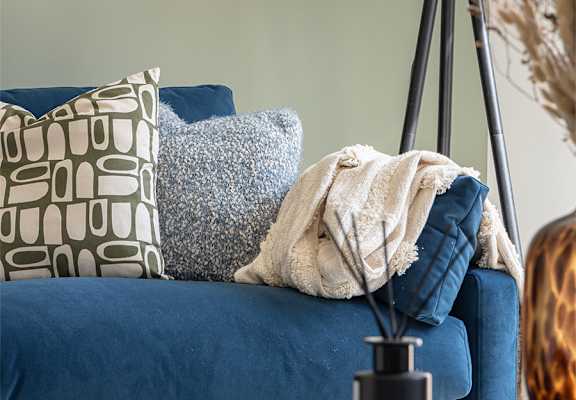 A blue couch with a grey cushion and a black and white pillow.