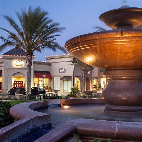 A large fountain is in the middle of a plaza in front of a building with palm trees.