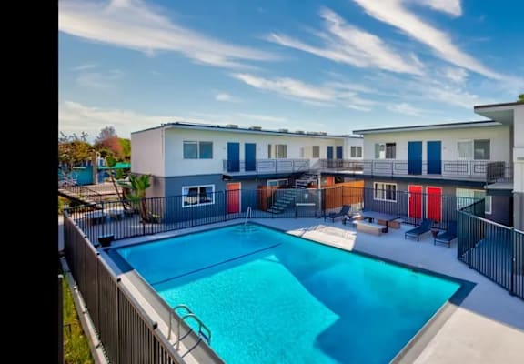 A swimming pool is surrounded by a fence and a building with multiple windows and doors.