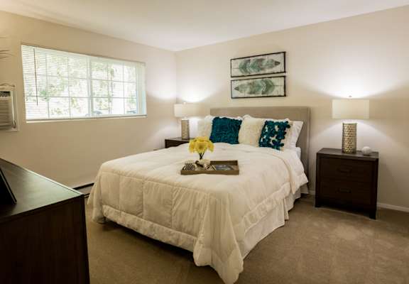 A bedroom with a bed, nightstand, and a plant.