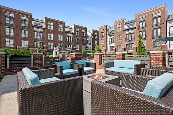 A patio with wicker furniture and a fire pit in front of apartment buildings.