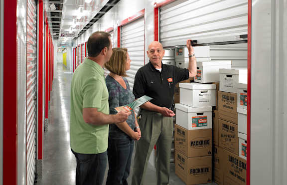 A man in a black shirt is holding a box while two other people look on.