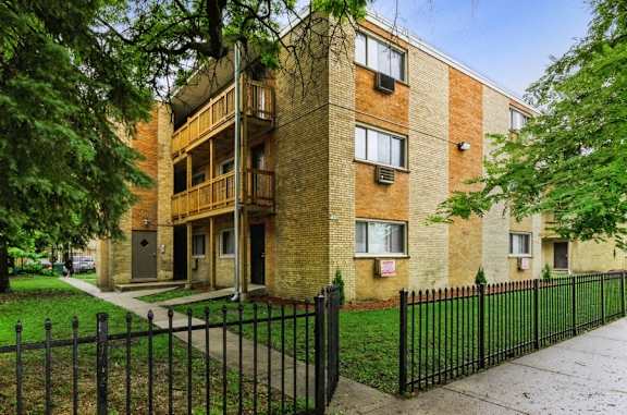 A brick apartment building with a black fence in front.