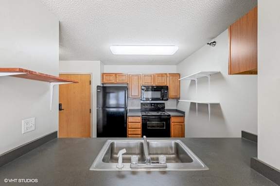 A kitchen with a black refrigerator, black oven, and black microwave.
