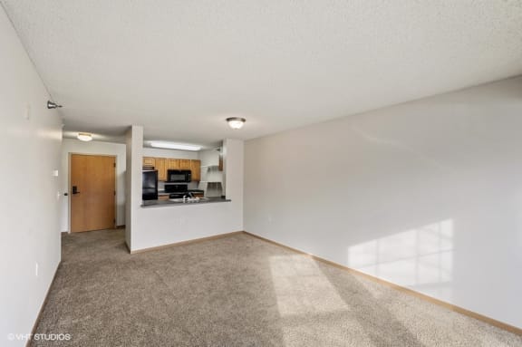 an empty living room with a kitchen in the background
