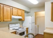 Thumbnail 3 of 31 - L Shaped Kitchen with Blonde Cabinets Tan Counters and White Appliances and Utility Closet with Washer Visible in the Background