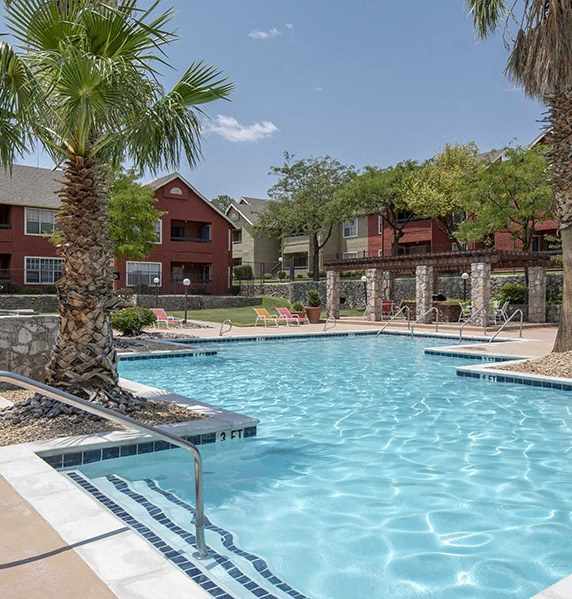 A pool surrounded by palm trees and a red building in the background.