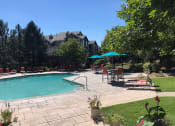 Thumbnail 40 of 40 - Westlake Greens Pool Deck with turquoise umbrellas, orange chairs, and green grass
