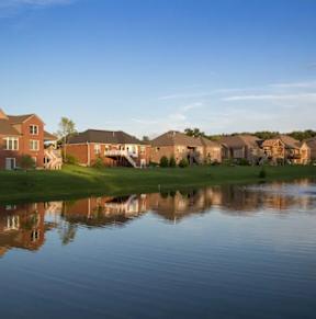 A serene lake in front of a row of houses with a fountain in the middle.