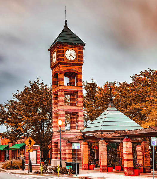 A clock tower stands in front of a building with a green roof.