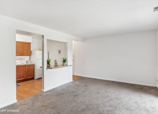 an empty living room with a kitchen in the background