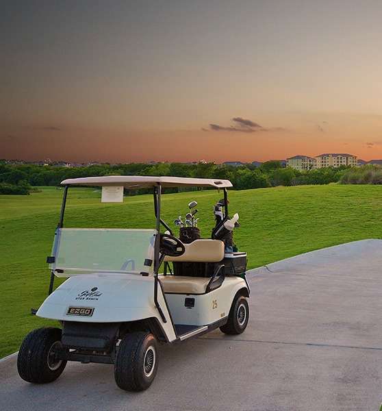 A golf cart is parked on a path with a sunset in the background.