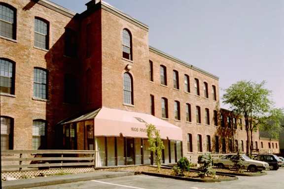 A red brick building with a pink awning and a tree in front.