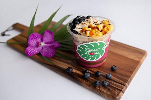 a cup of yogurt with fruit on a cutting board with a flower