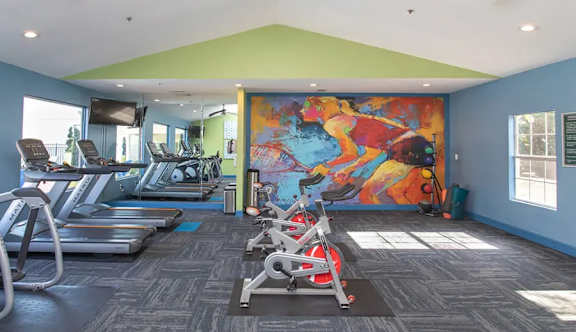 a gym with cardio machines and a colorful mural on the wall