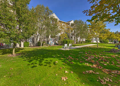A large building is behind a grassy area with trees and a benchat VINTAGE AT Sequim Apartments, Sequim ,Washington