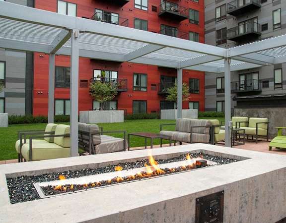 A fire pit in the middle of a patio with green chairs around it.