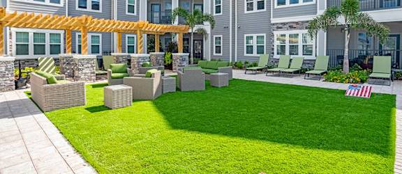 an outdoor lounge area with a grassy area and a large building in the background