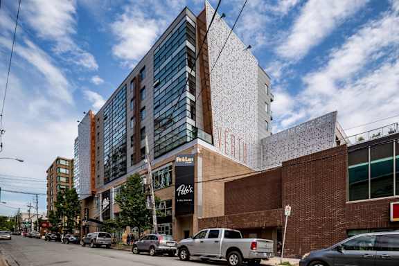 A modern building with a glass facade is located on a street with cars parked in front.