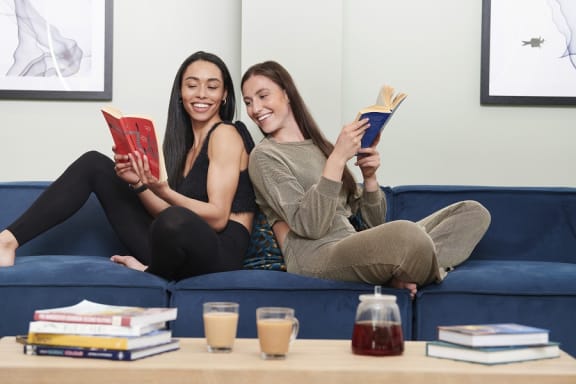 two women sitting on a couch reading books