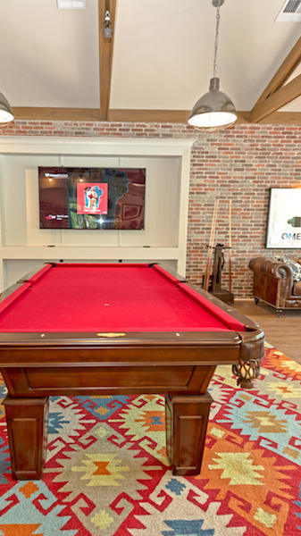 a red pool table in a living room with a brick wall at Midtown Sam Houston Apartments, Huntsville, TX, 77340