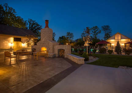 A stone fireplace is the centerpiece of a patio with wooden chairs.
