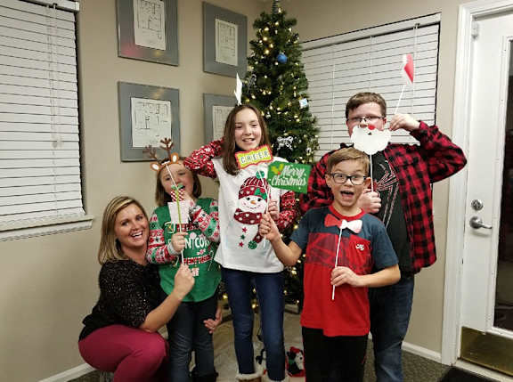 A family of five wearing Christmas sweaters and reindeer antlers posing for a photo.