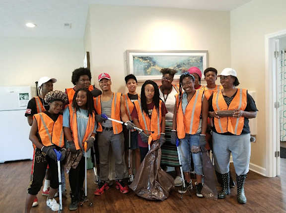 A group of people wearing orange vests and holding cleaning supplies.
