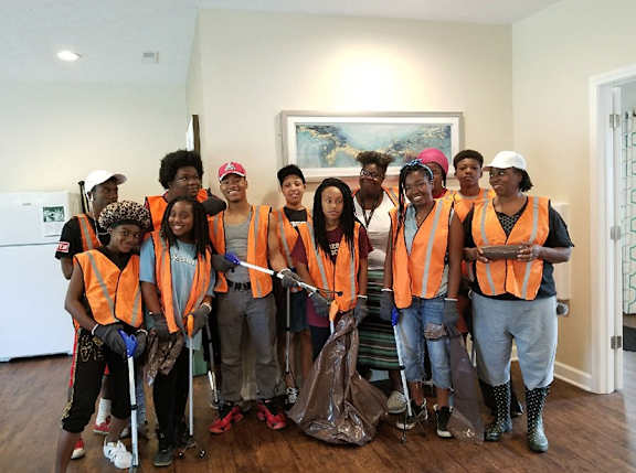 A group of people wearing orange vests and holding cleaning supplies.