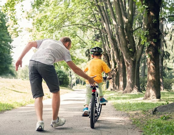 a man helping a boy ride a bike down a path