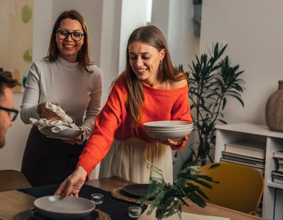 two women standing in a kitchen preparing food with plates