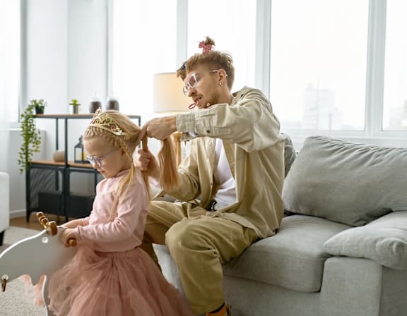 a mother and daughter sitting on a couch playing with their hair