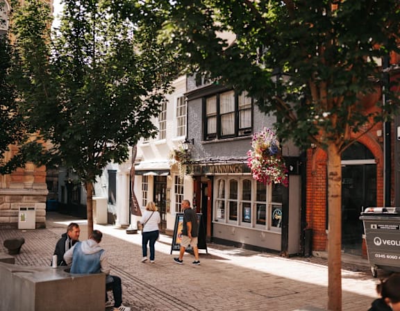 a city street with people walking and people sitting on a bench