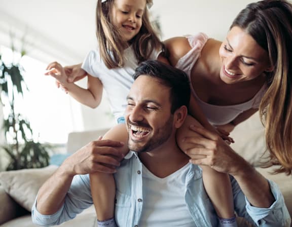 a man and woman sitting on a couch with a little girl on their husbands shoulders