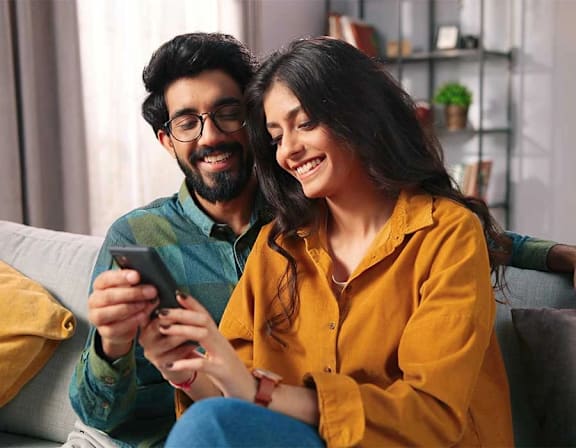 a man and woman sitting on a couch looking at a cell phone