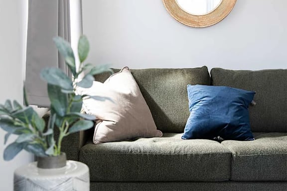 A grey couch with a round mirror and a vase with a plant on a table at UnionView Apartments, Dartford, KENT