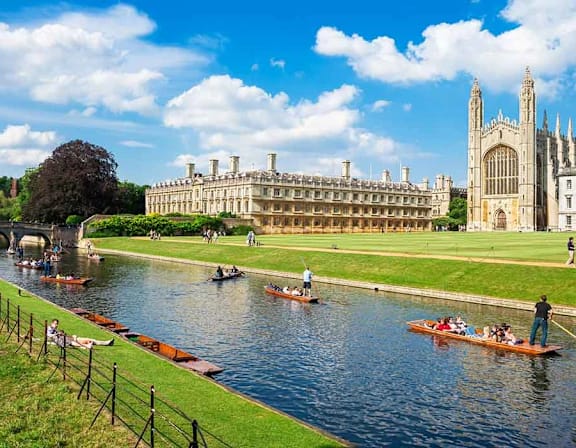 A group of people are rowing boats on a river in front of a large building. at Origins Apartments, Cambridge
