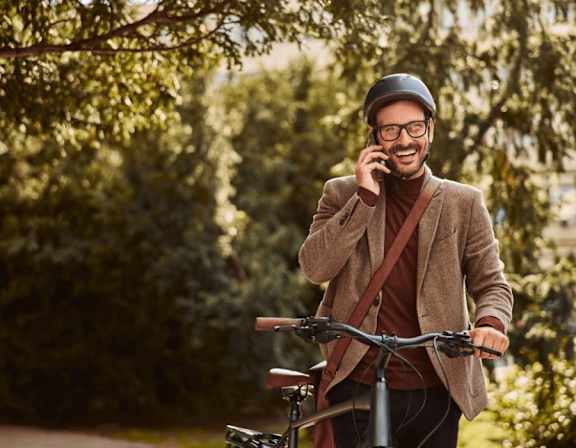 A man in a brown coat and hat is talking on a phone while holding a bicycle. at Origins Apartments, Cambridge
